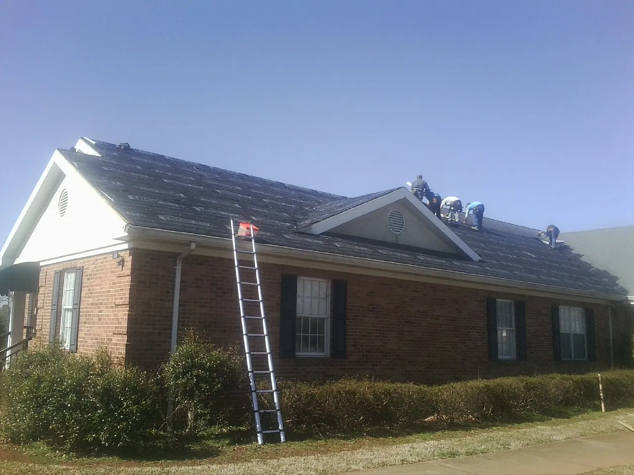 Crew tearing shingles off a brick ranch roof with a ladder set — Emergency Roof Repair work by our crew in Fultonham