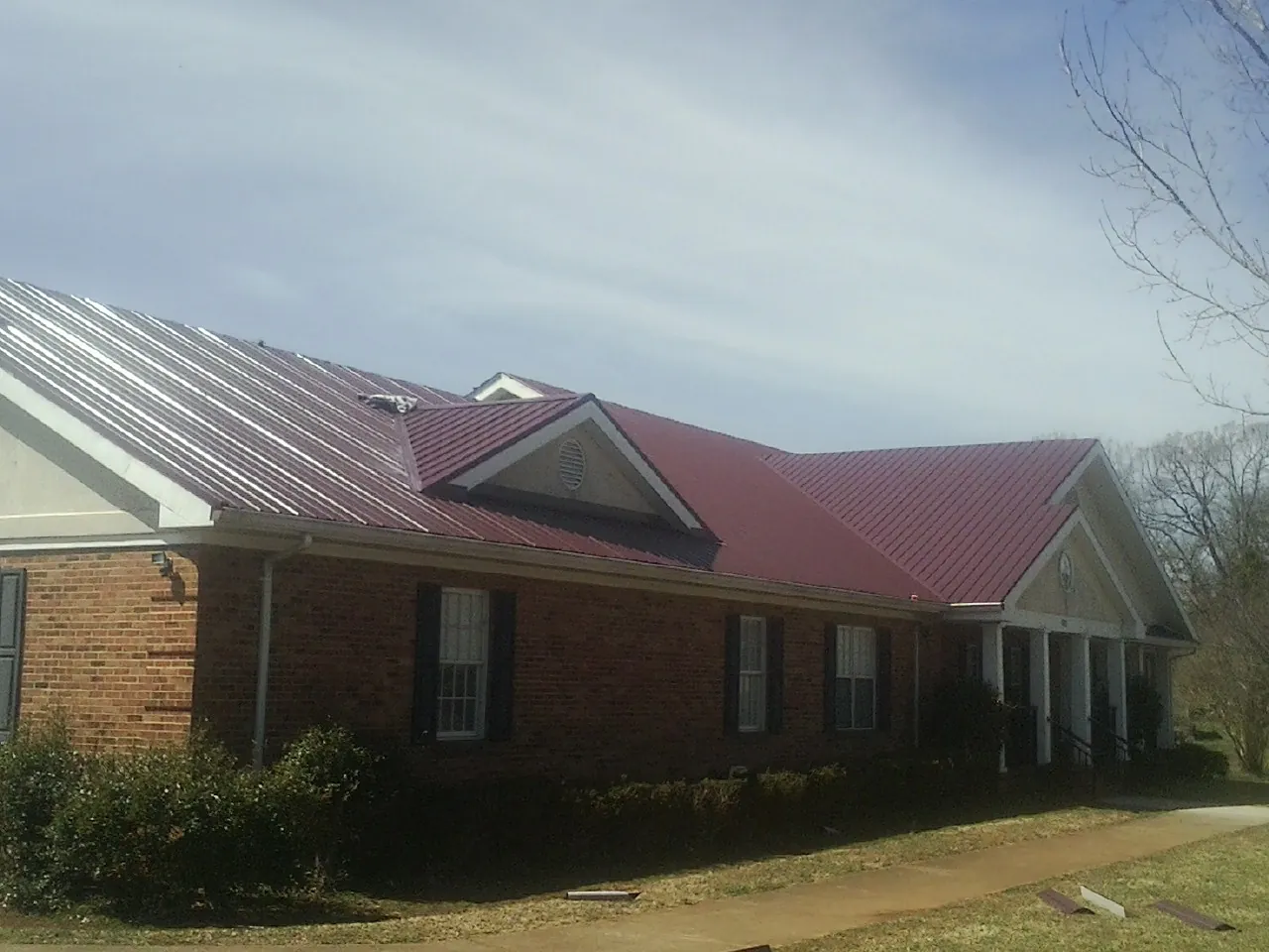 Red metal roof with gabled entries on a long brick building, from a Hail Damage Roof Repair job in Fultonham