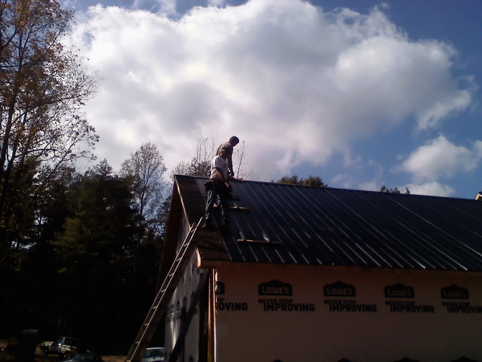 Roofer fastening dark metal panels high against a cloudy sky, from a Roof Inspection job in Fultonham